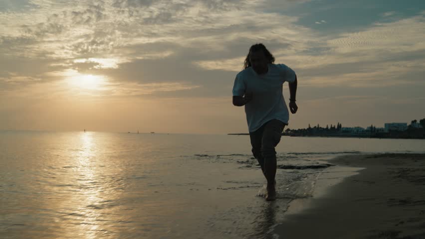 mid shot of young Male running on the beach in the water at sunrise slow motion