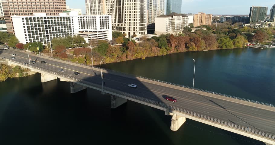 A slow reverse aerial view of traffic flowing over the S Congress Avenue Bridge over the Colorado River in downtown Austin, Texas on an early autumn evening.  	