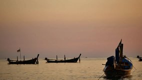Group of silhouette long tail boat converted to boat excursions floating in the andaman sea with golden light of the Sun before sunset and island background in travel or transportation concept