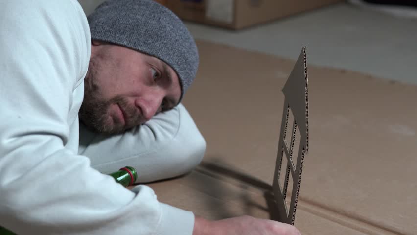 A homeless addict misses his family while holding a paper house in his hands. The housing crisis and the dream of happiness.