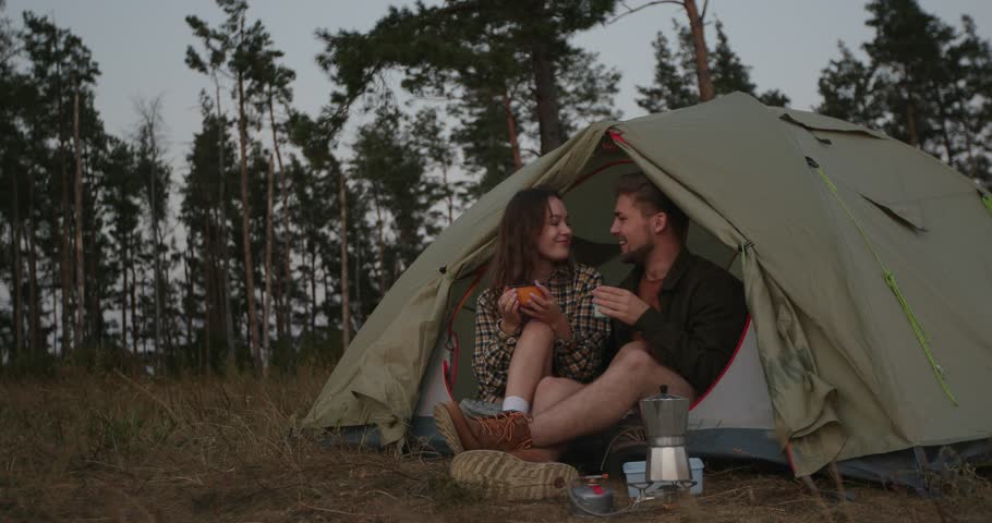 A young man and his girlfriend have dinner and make delicious coffee near a tent in the mountains after climbing. A couple in love rests near a tent at sunset. Royalty-Free Stock Footage #3417479011