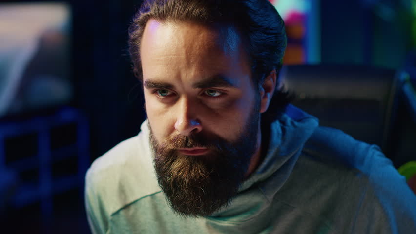 Focused streamer in neon illuminated apartment paying close attention to computer screen during competitive match. Pro gamer competing in online esports tournament, concentrating on incoming enemies