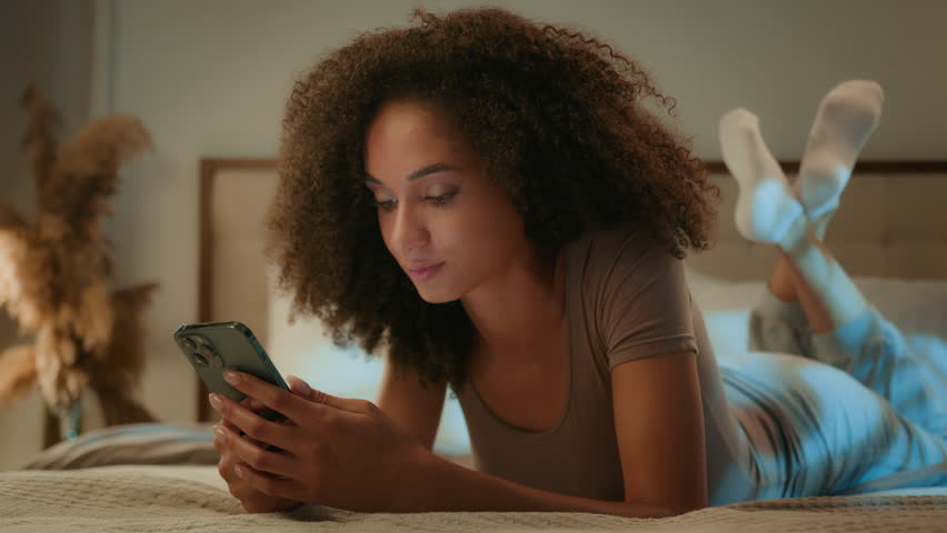 African American young woman shocked excited good news reading on mobile phone shock surprise wonder happy ethnic gen z girl lying with smartphone in bed rejoice amazing prize victory open mouth wow Royalty-Free Stock Footage #3417487177