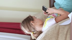 Cute little girl using technology device sitting on sofa. Girl playing on phone