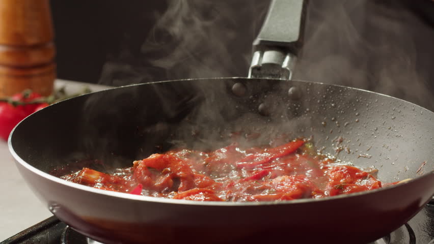 Tomatoes with red hot peppers, lime juice and shrimps are languishing in a pan. Traditional Asian Mexican Thai dish. High quality studio shot macro close-up. Cooking Italian pasta.