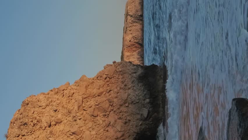 Zooming out of beautiful landscape of rock and sea waves of Fyriplaka beach, Milos, Greece at sunset