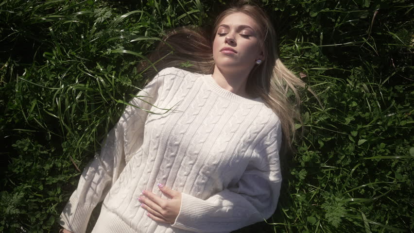 A girl lying on the ground strokes her knitted white sweater