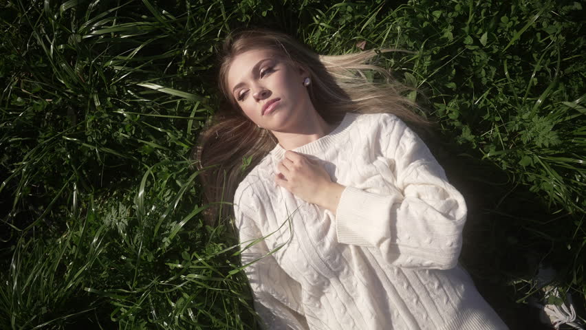 A girl lies on the grass with her hand pressed to her chest and looks at the sky