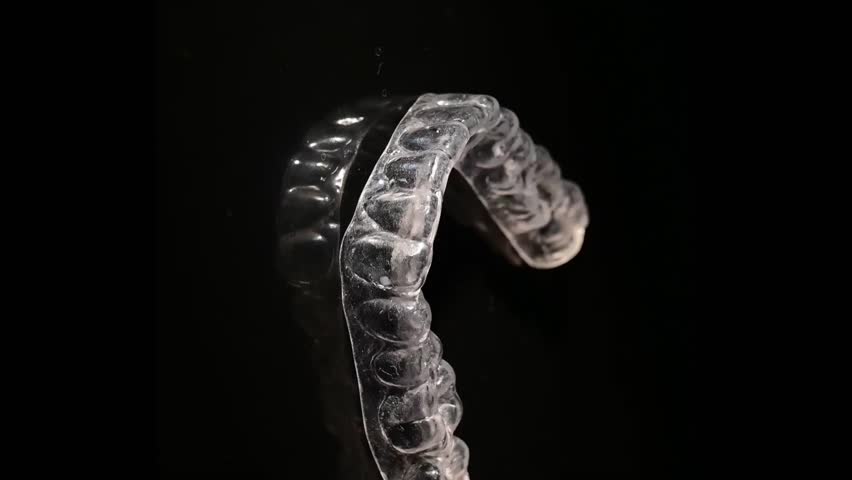 Transparent plastic mouth guard for bite alignment spins on a black background. Vertical video. 