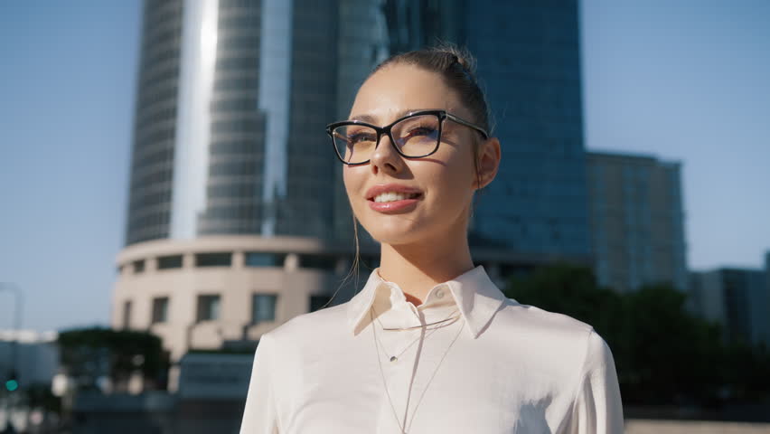 Happy young adult millennial girl smiling face with sleek bun hairdo wearing stylish glasses looking at camera posing outdoors at modern office building on background. Head shot close up portrait 4K Royalty-Free Stock Footage #3417608475