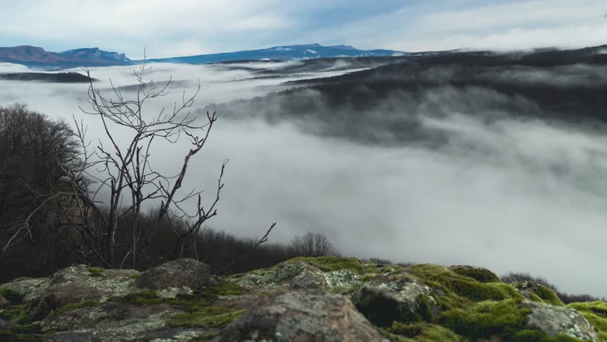 Sea of fog in a mountain valley. Time lapse. Autumn morning in the mountains. Mystical view from the top of a cliff. Smooth camera movement backwards. The beauty of the wilderness