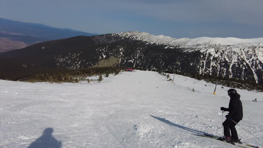 Male skier dressed in black, man skiing down a mountain piste or slope with a chair lift in the background 4K Stabilised Video Clip