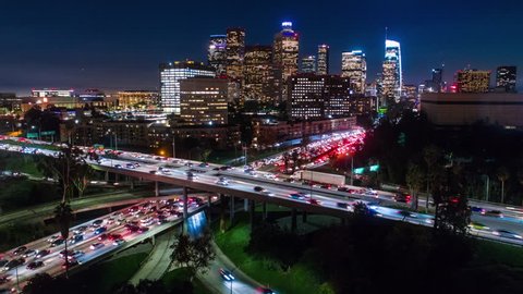 Cinematic urban aerial time lapse in motion of downtown Los Angeles freeways with heavy traffic, city skyline and sky scrapers at night with deep blue sky
