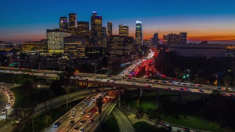 Cinematic urban aerial hyperlapse of downtown Los Angeles freeways and traffic with city skyline and skyscrapers at sunset with deep blue and orange colors.