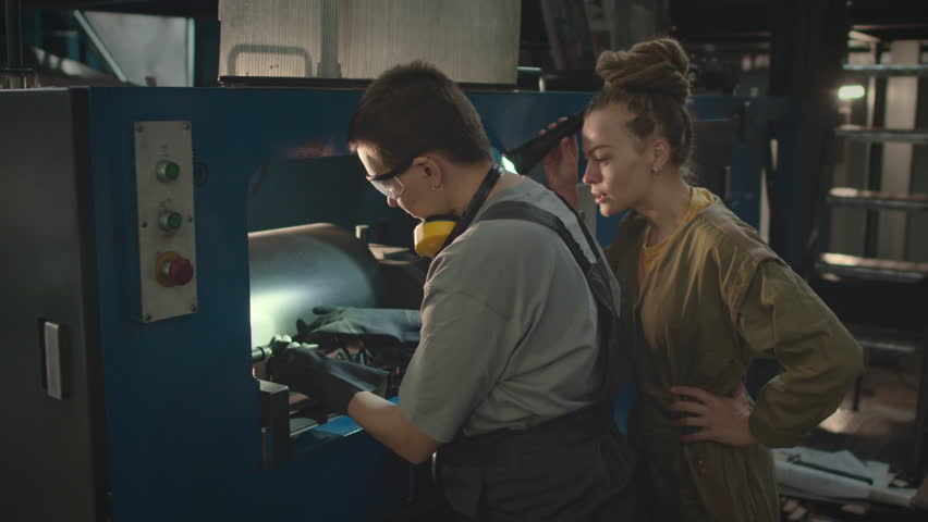 Medium shot of Caucasian short haired female industrial machinery equipment using metal t-spanner and speaking with coworker while repairing machine at factory Royalty-Free Stock Footage #3417832269