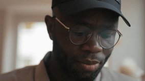 Portrait of a serious face of an African American man, looking at the camera, wearing glasses and a cap, close-up, handsome, confident lifestyle, in a cafe, attractive, slow motion.