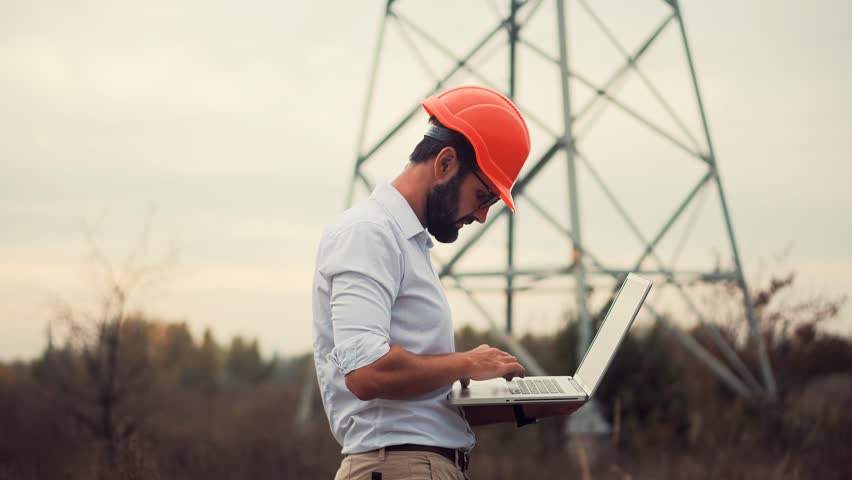 Constructor Inspect High Voltage Tower.Engineer In Hard Hat Maintenance Electricity Transmission Pylon.Electrical Engineer In Helmet Power Line.Constructor Checking High Voltage Sensor Power Line Wire