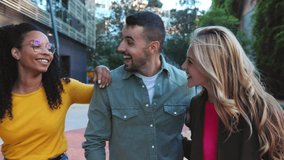 Three happy young adult friends laughing together bonding at city street. Diverse millennial people having fun, enjoying free time outdoors. Friendship and youth concept. Slow motion footage.
