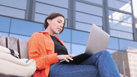 Confident woman having video meeting by laptop while sitting on bench over glassy building background. Remote HR manager conducting interview with candidate and explaining working conditions.