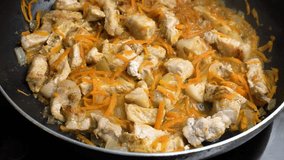 Pieces of pork meat are stewed in a frying pan with onions and grated carrots in sizzling oil. Cooking meat goulash. Close-up. Suitable for content about home cooking, recipe videos, cooking skills.