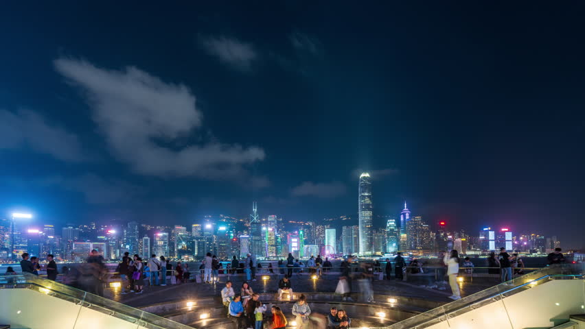 HONG KONG, CHINA - 25 November 2023: Time lapse of pedestrians crowding Avenue of Stars at night with Central Hong Kong skyline in the background, vibrant city lights, urban motion, tourism hotspot
