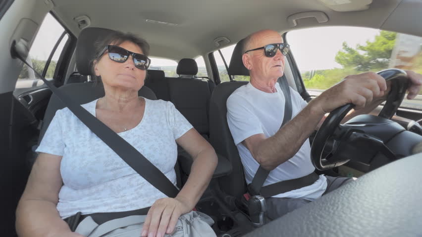 happy old man and woman having fun together while traveling on vacation dancing and singing while driving a car