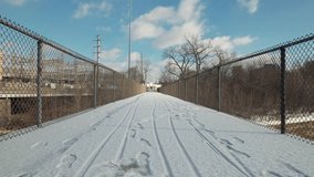 Point-of-view stabilized view of snow and ice covered bike and hiking trail and path on city pedestrian bridge near downtown Columbus, Ohio with footprints