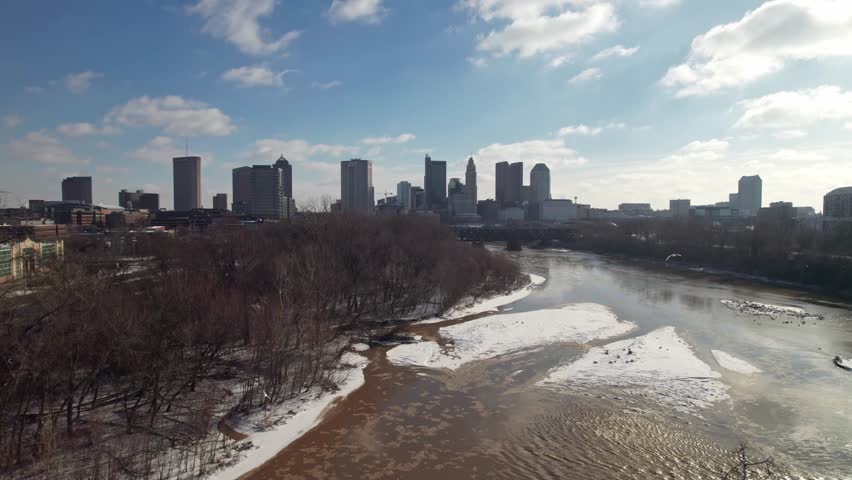 Drone aerial of Columbus, Ohio state capital city in January winter storm, covered in snow, ice, and frozen ground and Scioto river leading towards downtown buildings, government offices, and roads