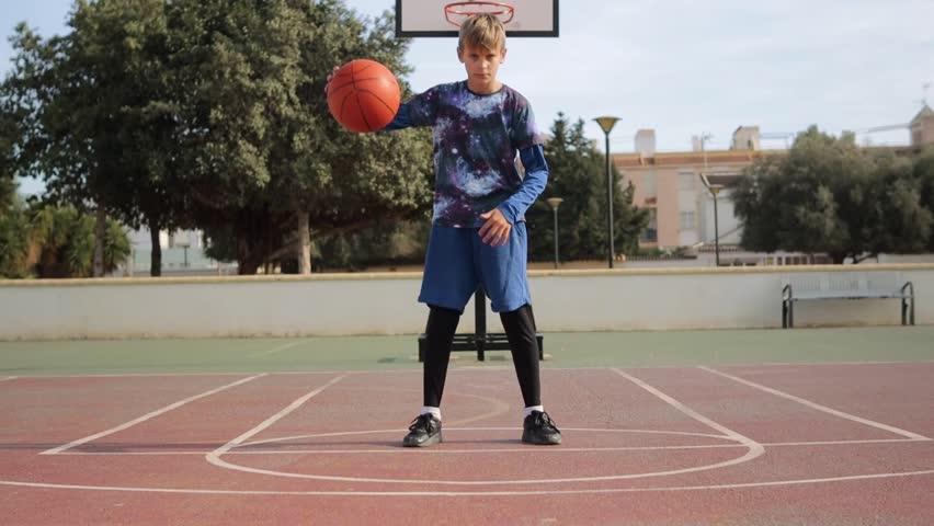 boy playing basketball in playground, throws the ball into basket at sunset in front of the camera Royalty-Free Stock Footage #3418119215
