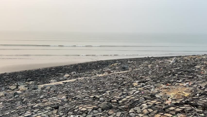 Cinematic shot of a shore line covered with stones near an ocean in Tajpur, Bengal, India
