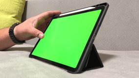 Tablet with green screen and man's hand. Male hand holding tablet with green screen. A man is resting at home and playing computer games. Home Interior, Work and Leisure. Smart technology.