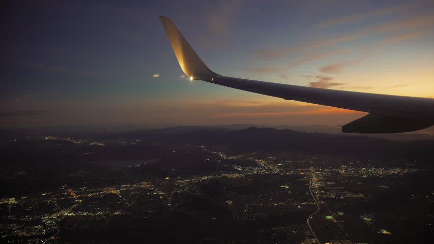 Airplane Jet plane prepare to landing in Los Angeles LAX airport. Porthole view with wing on sunset. Slow motion