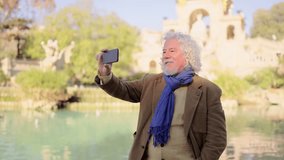 Video of a senior man in a video call next to an urban lake in a park