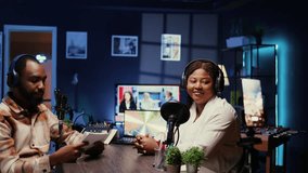 African american host using smartphone on tripod to record entertaining discussion with woman during livestream in apartment studio. Presenter uses mobile phone camera to produce comedy podcast