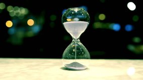 A few sand falling in hourglass on a table with blur background. A close up of hourglass showing passage of time. The hourglass pouring out the sand on the desk. Time flows, the transience of time.