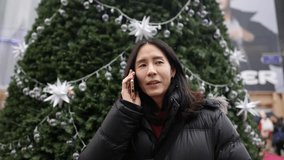Slow-motion video of a Korean man in his 30s talking on his smartphone in front of a Christmas tree in the cold winter in Myeong-dong, Seoul, South Korea