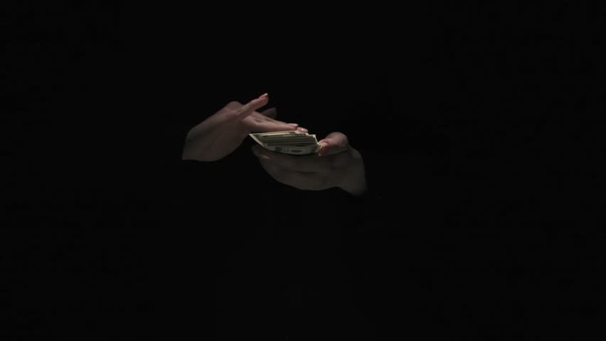 Portrait of female in black suit isolated on black background in low light. Woman holding wad of dollar banknotes in hand and throwing notes in air. Royalty-Free Stock Footage #3418548155