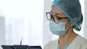 Doctor woman at work using a clipboard while writing medical notes. Nurse standing near the window in hospital and writing notes, close-up. 4k slow motion