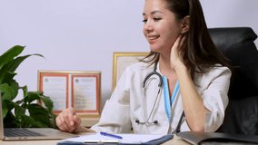 Female doctor talking with her patient remotely via telemedicine from her medical office. Woman doctor sitting at table and using laptop for online meeting, 4k slow motion