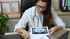 Dentist doctor or nurse in uniform holding X Ray while sitting at laptop computer. Online medical consultation