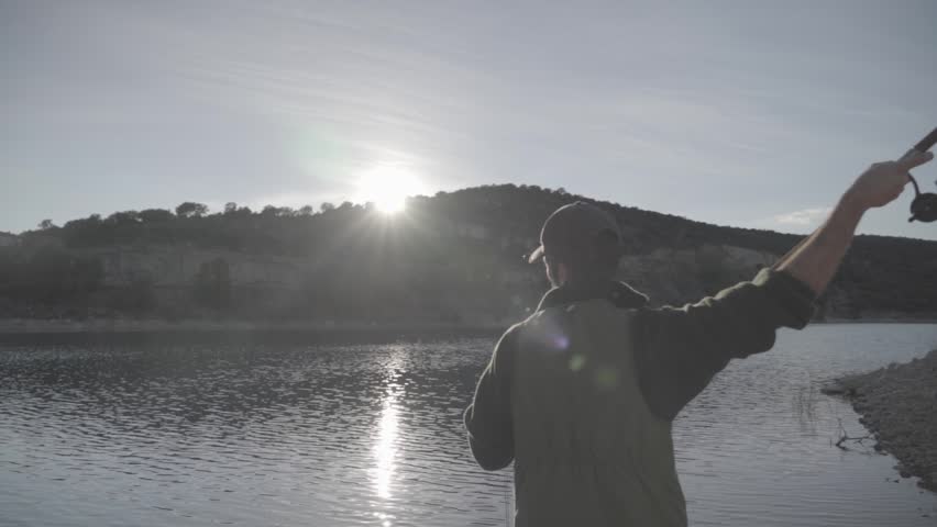 Fisherman casting a rod into a lake at sunset