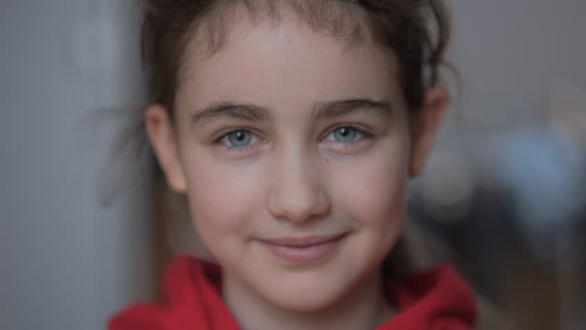 Portrait of Teenage Girl with Blue Eyes in Red Hoodie Looks at Camera. Portrait Funny Little Girl Smiling Child. Face Contemplative Child Cute Pretty Schoolgirl Elementary Student. Positive Emotions.