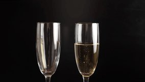 Champagne is poured into glasses on a black background. Slow motion.