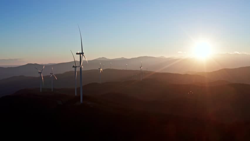 Sunset illuminating wind turbines on rolling hills, captured from an aerial perspective emphasizing renewable energy