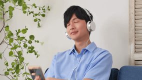 Asian man listening to music on his smartphones in the living room