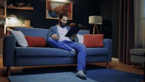 Cheerful man relaxing at home. Male sitting at sofa with crossed legs. Man holding tablet and smiling. Male wearing glasses and looking at tablet. Man having spare time at home. Staying at home. - Powered by Shutterstock - Get 15% off with code: PIKWIZARD15