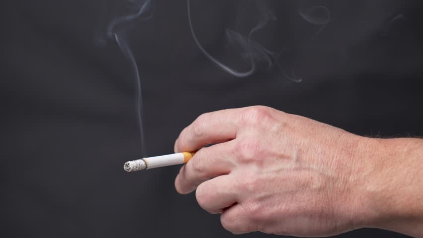 Smoking a cigarette. Male hand holding cigarette on black background with copy space,close-up. 4k slow motion