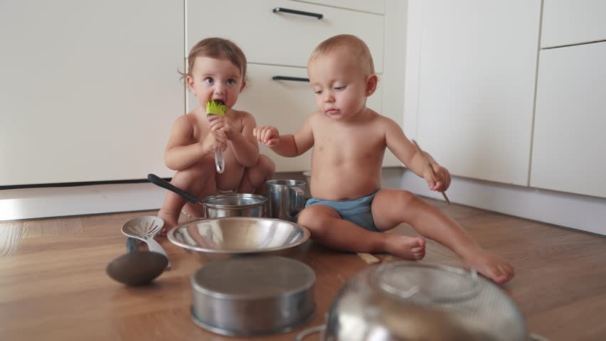 baby group playing pots in the kitchen on the floor. happy family kid dream concept. two baby twins scattered pots lifestyle play dabble sitting on floor. baby scattered dishes pots mess Royalty-Free Stock Footage #3418875917