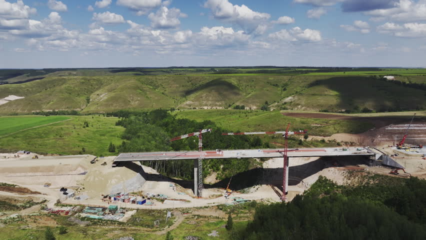 Construction cranes located in bridge work area surrounded by nature. Process of bridge building among mountainous terrain away from city Royalty-Free Stock Footage #3418881309