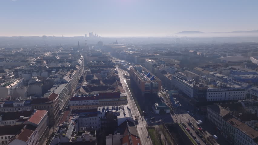 Aerial panoramic view of wide boulevards in large city. View against sunshine in morning haze. Traffic on roads. Vienna, Austria